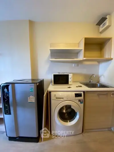 Compact kitchen with washing machine, fridge, and microwave in modern apartment.