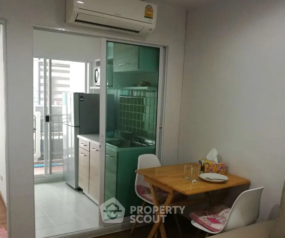 Cozy dining area with compact kitchen and balcony view in modern apartment.