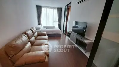 Modern living room with cozy leather sofa and large TV, featuring a bright window view.