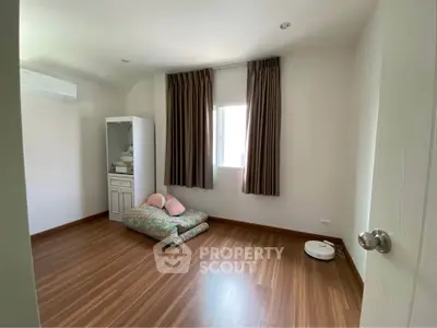 Spacious bedroom with wooden flooring and natural light, featuring a minimalist design and air conditioning.