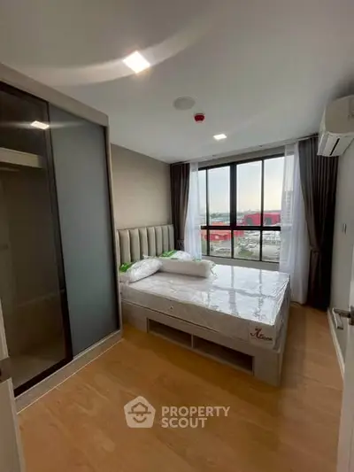 Modern bedroom with large window and city view, featuring a comfortable bed and sleek design.
