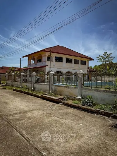 Charming two-story house with red roof and spacious fenced yard, perfect for family living.