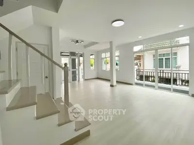 Spacious modern living room with large windows and elegant staircase in a bright home.