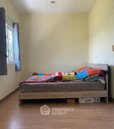 Cozy bedroom with natural light and wooden flooring, perfect for relaxation.