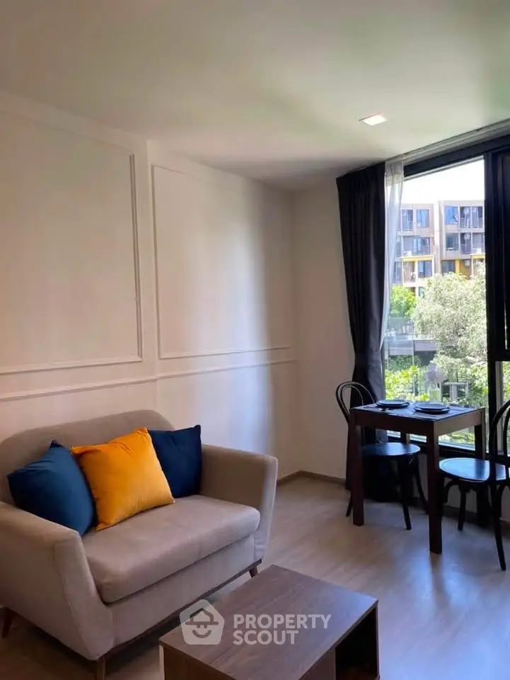 Charming living room with cozy sofa and dining area, featuring large window with garden view.