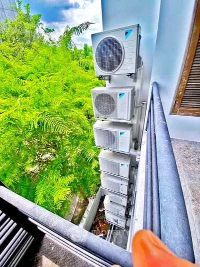 Modern apartment balcony with stacked air conditioning units and lush greenery view.