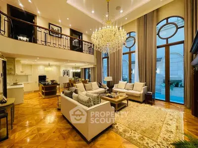 Luxurious living room with high ceilings, elegant chandelier, and large windows overlooking a pool.