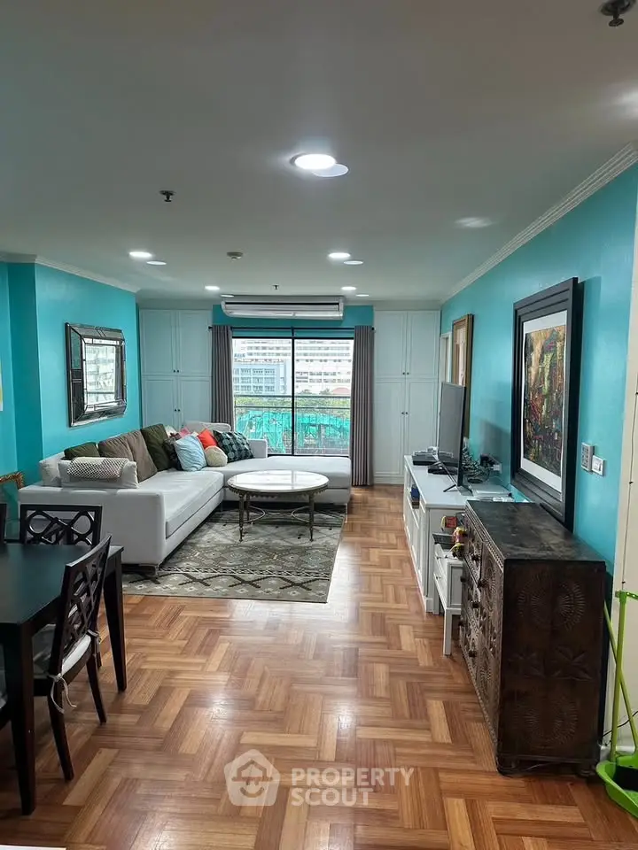 Spacious living room with modern decor and city view, featuring parquet flooring and vibrant teal walls.