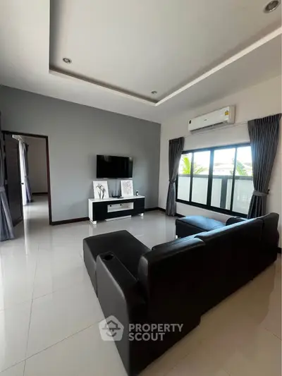 Spacious modern living room with sleek black sofa and large windows for natural light.