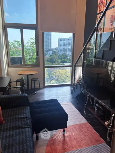 Modern living room with large windows and city view, featuring stylish furniture and a staircase.