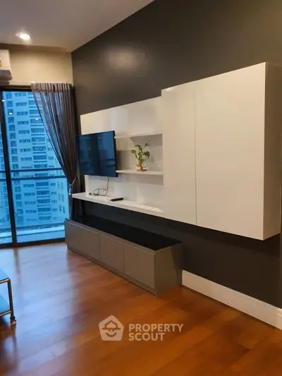 Modern living room with sleek wall-mounted TV and stylish cabinetry, featuring a large window with city view.