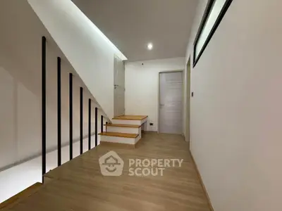 Modern hallway with wooden flooring and sleek staircase in contemporary home.