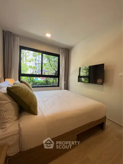 Cozy bedroom with large window and garden view, featuring modern decor and wall-mounted TV.