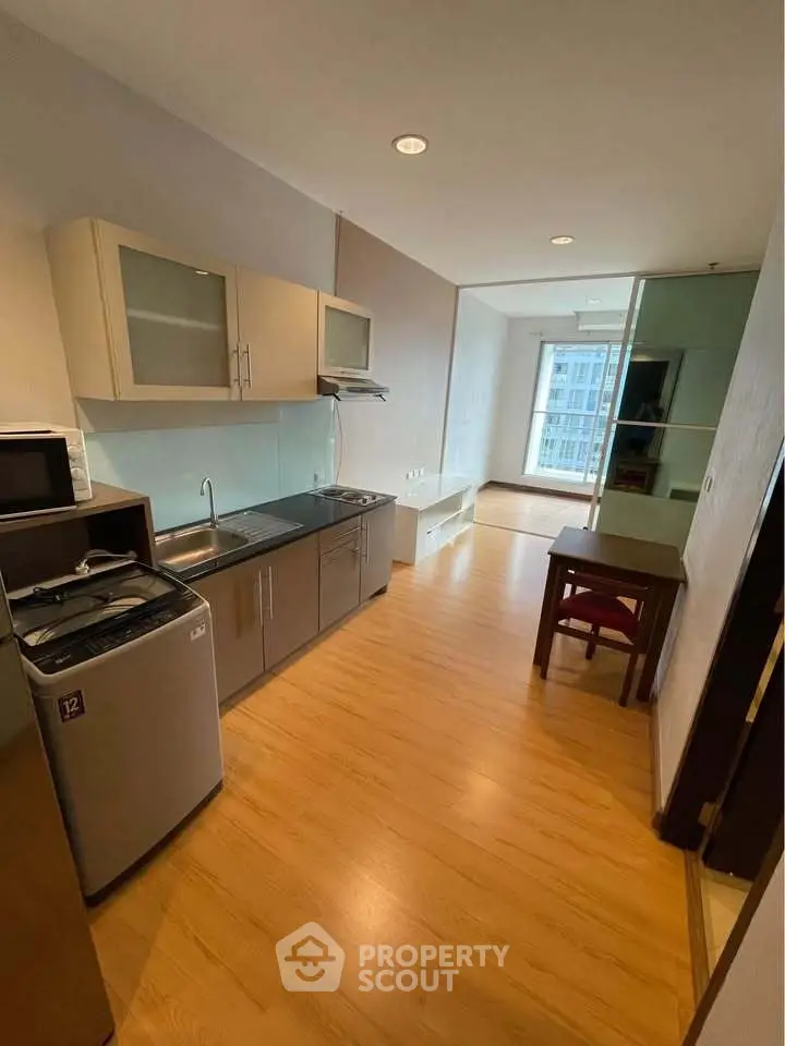 Modern studio apartment with kitchenette and dining area, featuring sleek wooden flooring and ample natural light.