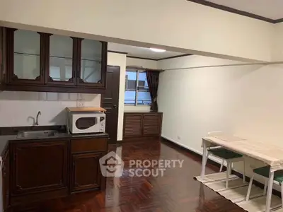 Charming open-layout living space with kitchenette and dining area, featuring wooden flooring and ample natural light.