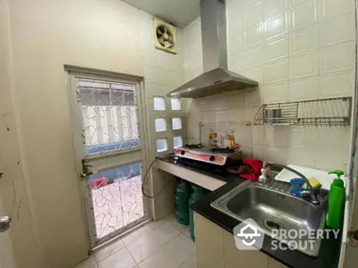 Compact kitchen space with tiled walls, stainless steel sink, and window providing natural light, ideal for urban living.