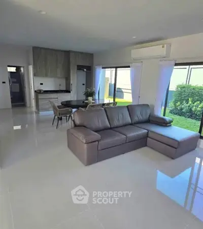 Spacious modern living room with open kitchen and garden view, featuring sleek furniture and abundant natural light.