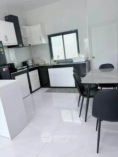 Modern kitchen with sleek white cabinets and dining area, featuring a stylish marble table and black chairs.