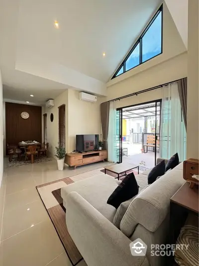 Spacious modern living room with high ceiling and large windows, open layout to dining area, stylish decor.