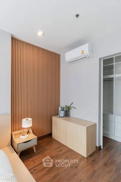 Modern bedroom with sleek wooden paneling and air conditioning, featuring a stylish lamp and storage unit.