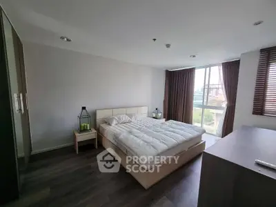 Spacious bedroom with modern decor and large window offering natural light and city view.