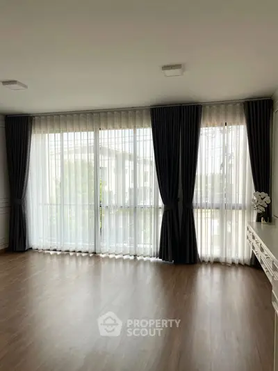 Spacious living room with large windows and elegant curtains, offering abundant natural light and a serene ambiance.