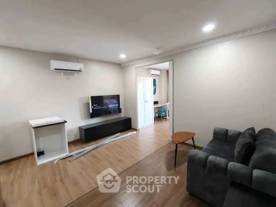 Modern living room with sleek furniture and wooden flooring, featuring a wall-mounted TV and air conditioning.