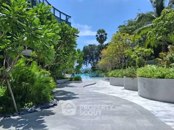 Luxurious garden pathway leading to a serene pool with lush greenery and ocean view.