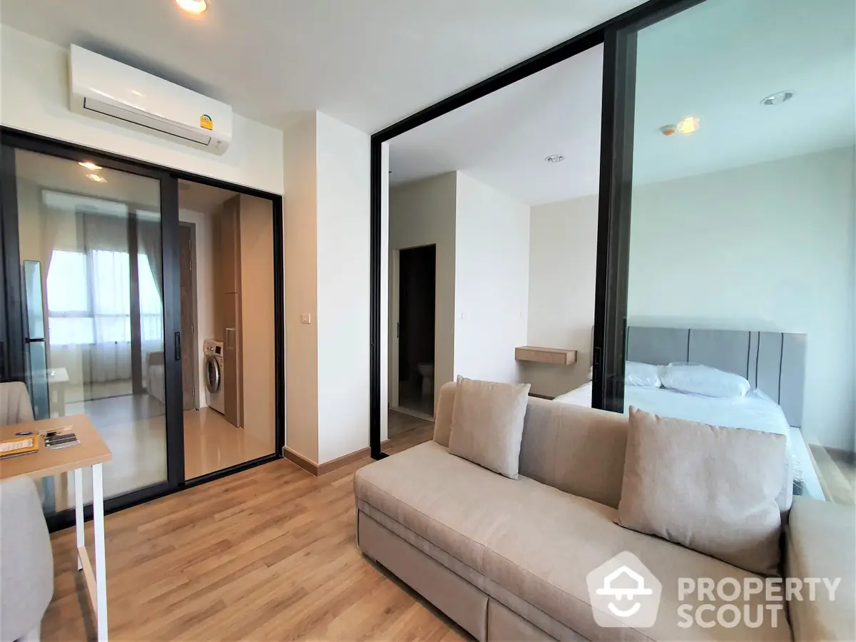 Modern apartment interior with a spacious living room connected to a cozy bedroom through glass sliding doors, featuring sleek furniture and a harmonious color palette.