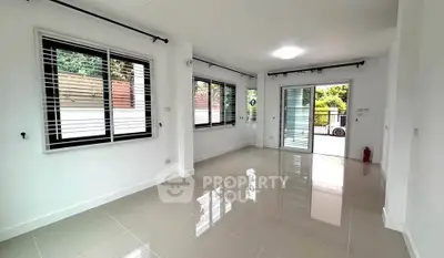 Spacious living room with glossy tiles and large windows opening to a garden view.