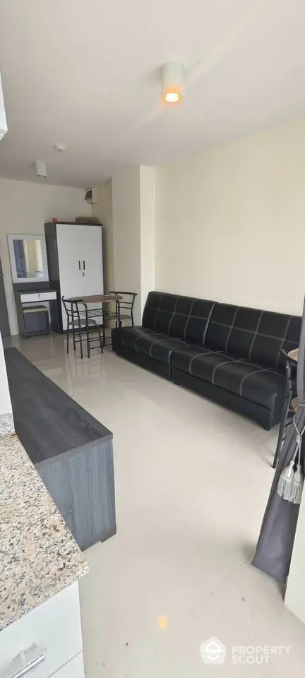 Modern living room with sleek black sofa and dining area in open layout apartment.