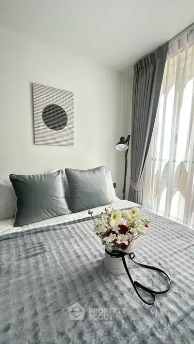 Elegant bedroom with plush bedding and stylish decor, featuring a large window with sheer curtains.