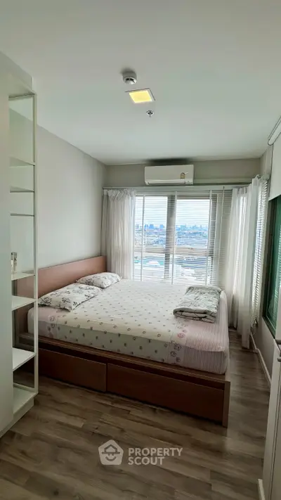 Cozy bedroom with city view, featuring a large bed and natural light through wide windows.