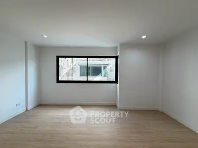 Spacious empty room with large window and wooden flooring, ideal for customization.