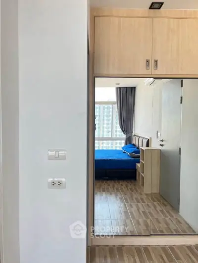 Modern bedroom with wooden flooring and large mirrored wardrobe reflecting a city view.