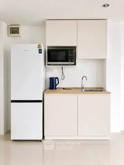 Modern minimalist kitchen with sleek cabinetry, fridge, microwave, and sink in compact layout.