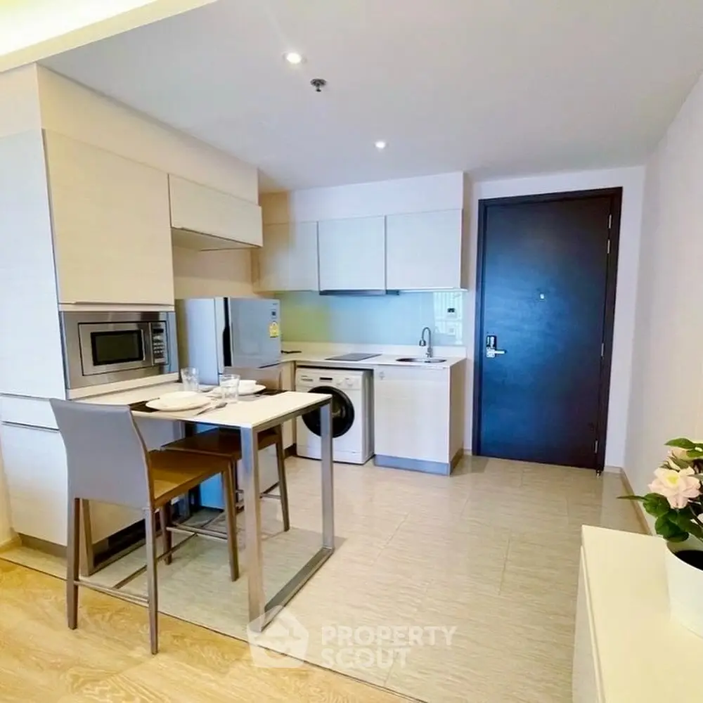 Modern kitchen with sleek cabinetry, washing machine, and dining area in compact apartment.