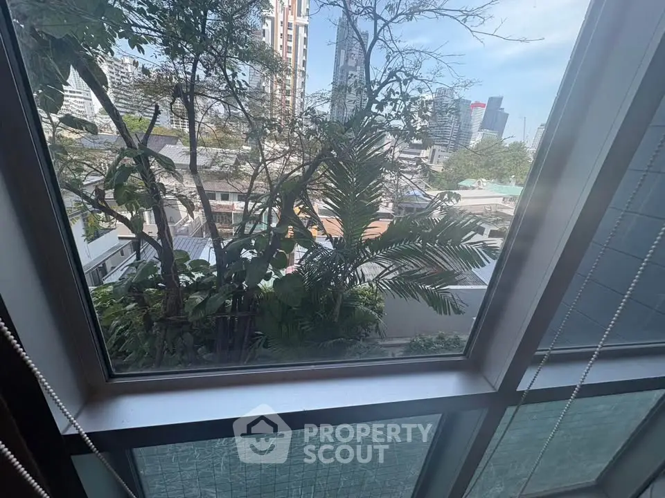 Stunning cityscape view from a modern apartment window, showcasing lush greenery and urban skyline.