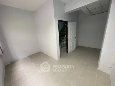 Spacious empty room with tiled flooring and open door leading to staircase.