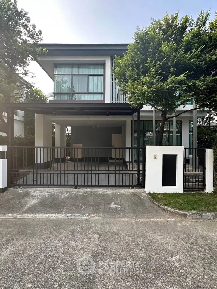 Modern two-story house with large windows and gated driveway in a serene neighborhood.