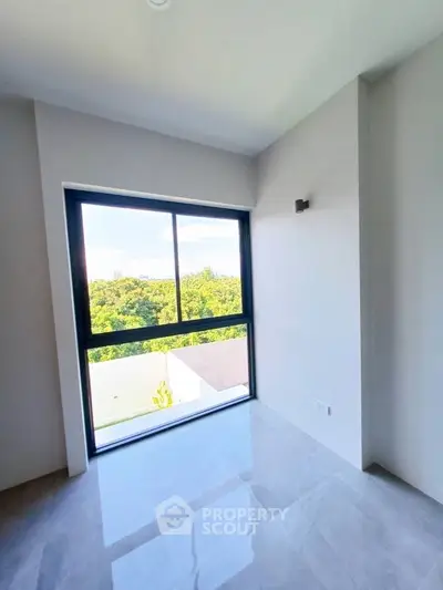 Bright room with large window offering lush green view, perfect for a serene living space.