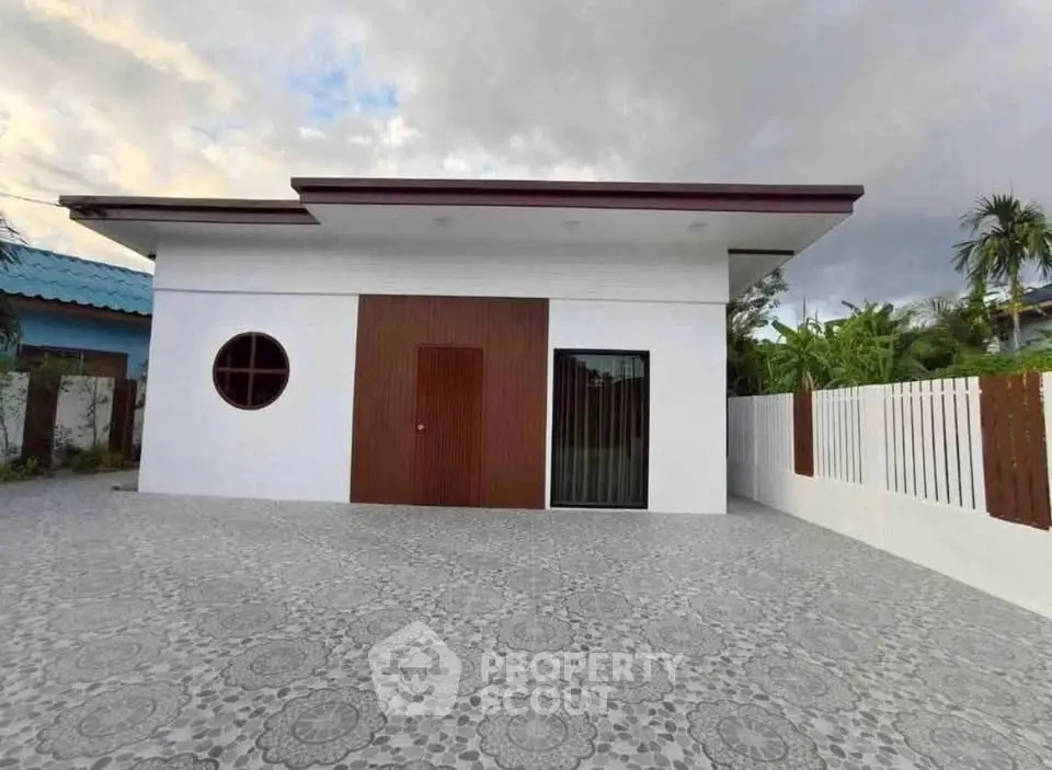 Modern minimalist house exterior with unique circular window and spacious patterned driveway.