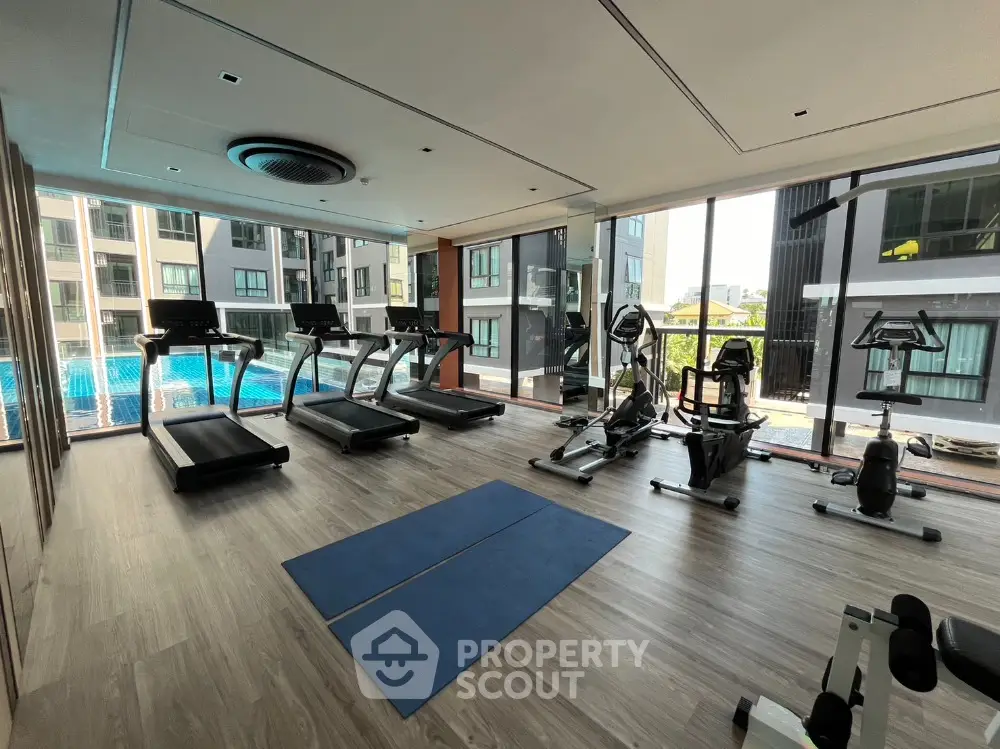 Modern gym with large windows overlooking pool in luxury apartment complex