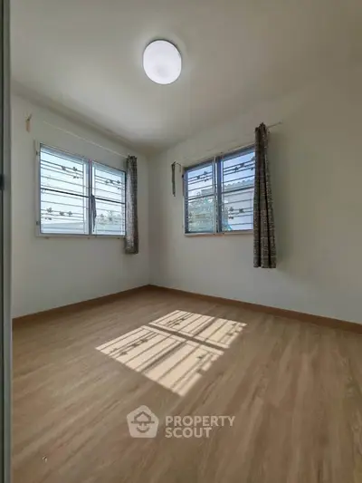Bright empty bedroom with wooden flooring and large windows, perfect for natural light lovers.