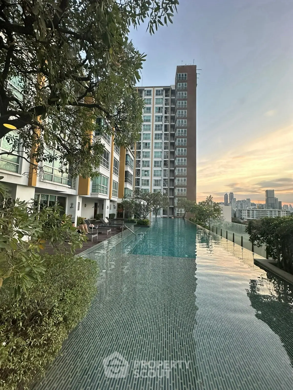 Luxurious high-rise apartment with stunning infinity pool and city skyline view at sunset.
