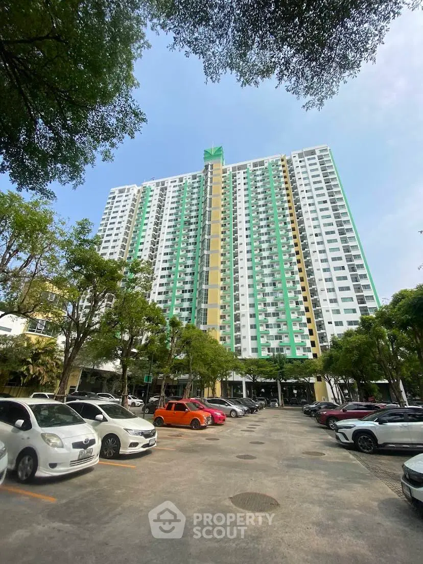Modern high-rise residential building with spacious parking area and lush greenery.