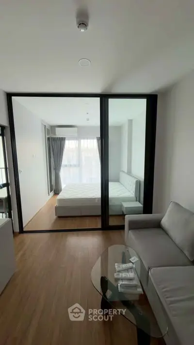 Modern apartment interior with glass partition, featuring a cozy living room and bright bedroom.