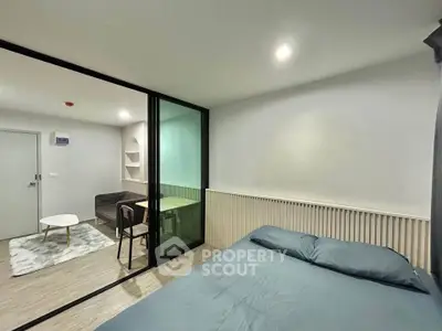 Modern bedroom with glass partition leading to cozy living area, featuring stylish decor and ample natural light.