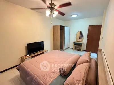 Spacious bedroom with modern decor and ceiling fan, featuring a cozy bed and entertainment setup.