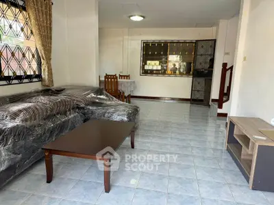 Spacious living room with tiled floor and large windows, featuring a cozy sofa and elegant wooden furniture.